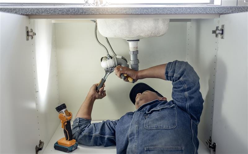 Plumber repairing pipes beneath a bathroom sink in Redlands