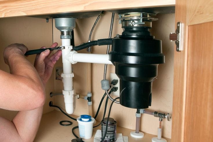 Plumber installing a garbage disposal beneath a kitchen sink in Redlands