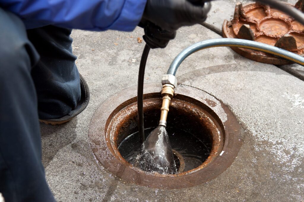 Plumber hydro jetting a sewer line through a manhole in Redlands