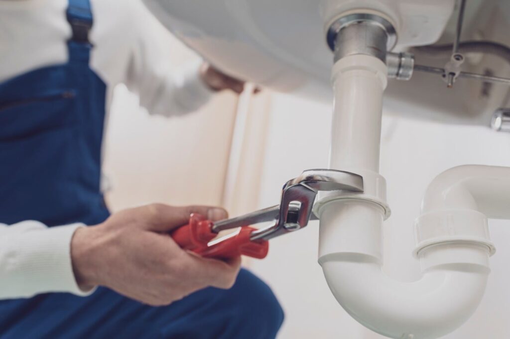 Plumber repairing a white drain pipe beneath a sink in Redlands