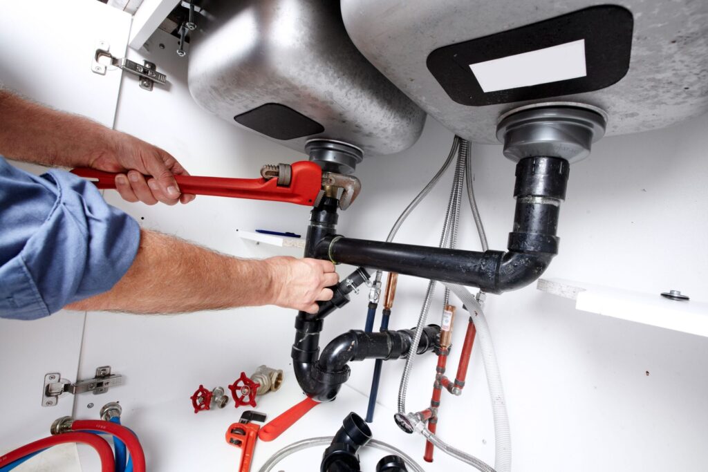 Plumber repairing drain pipes beneath a kitchen sink in Redlands